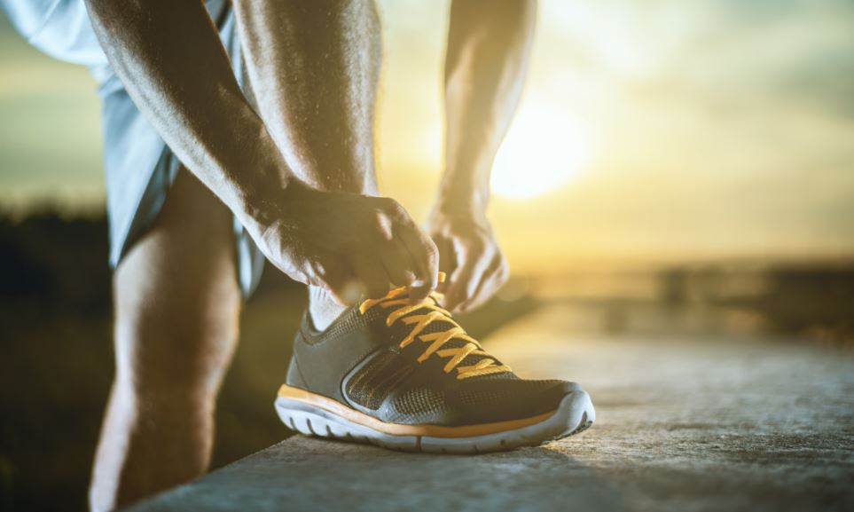 Homem praticante de corrida amarrando o tênis ao nascer do sol