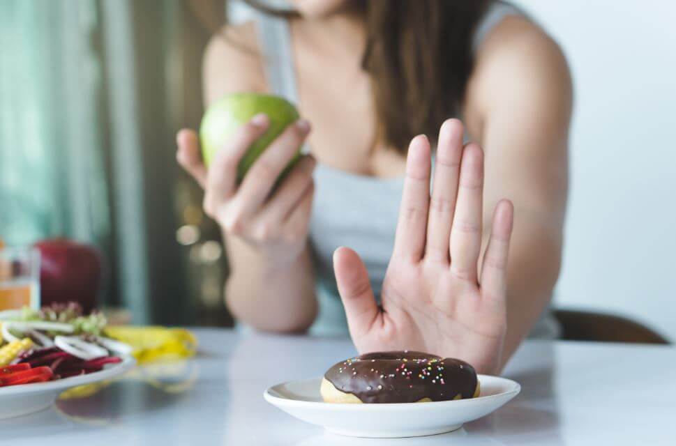 Mulher negando uma rosquinha e comendo uma maçã