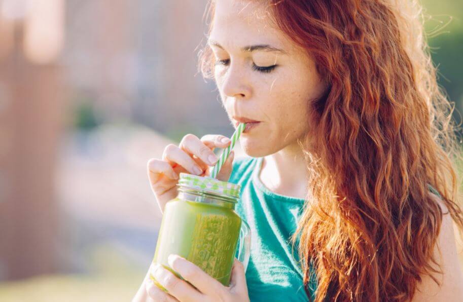 Menina tomando um suco verde com canudo