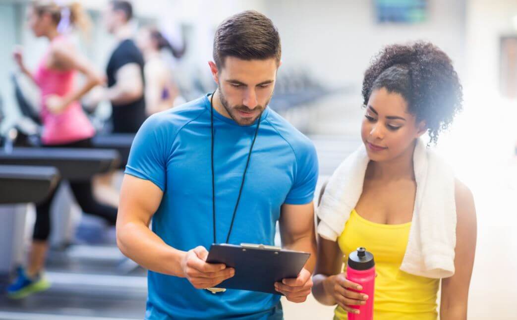 Professor mostrando treino para uma aluna na academia
